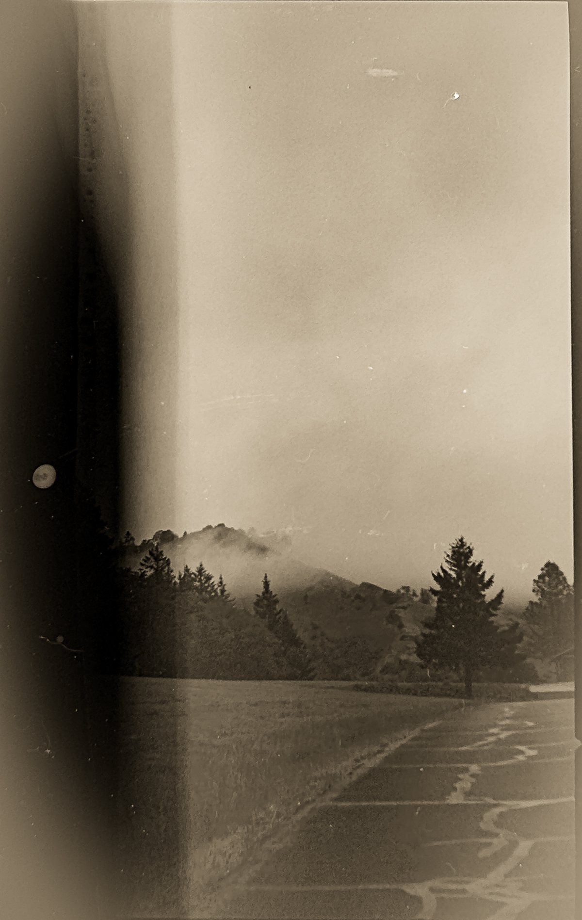 Two alternating monochromatic images that have the left edge completely undeveloped. The first image is a road and a hill with mist. The second image is a wooden shed.